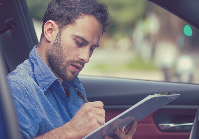 Mand sidder i bil med tjekliste En mand sidder i en bil med en tjekliste, hvor kan tjekker bilen tilstand af ved opkøb af brugte biler
